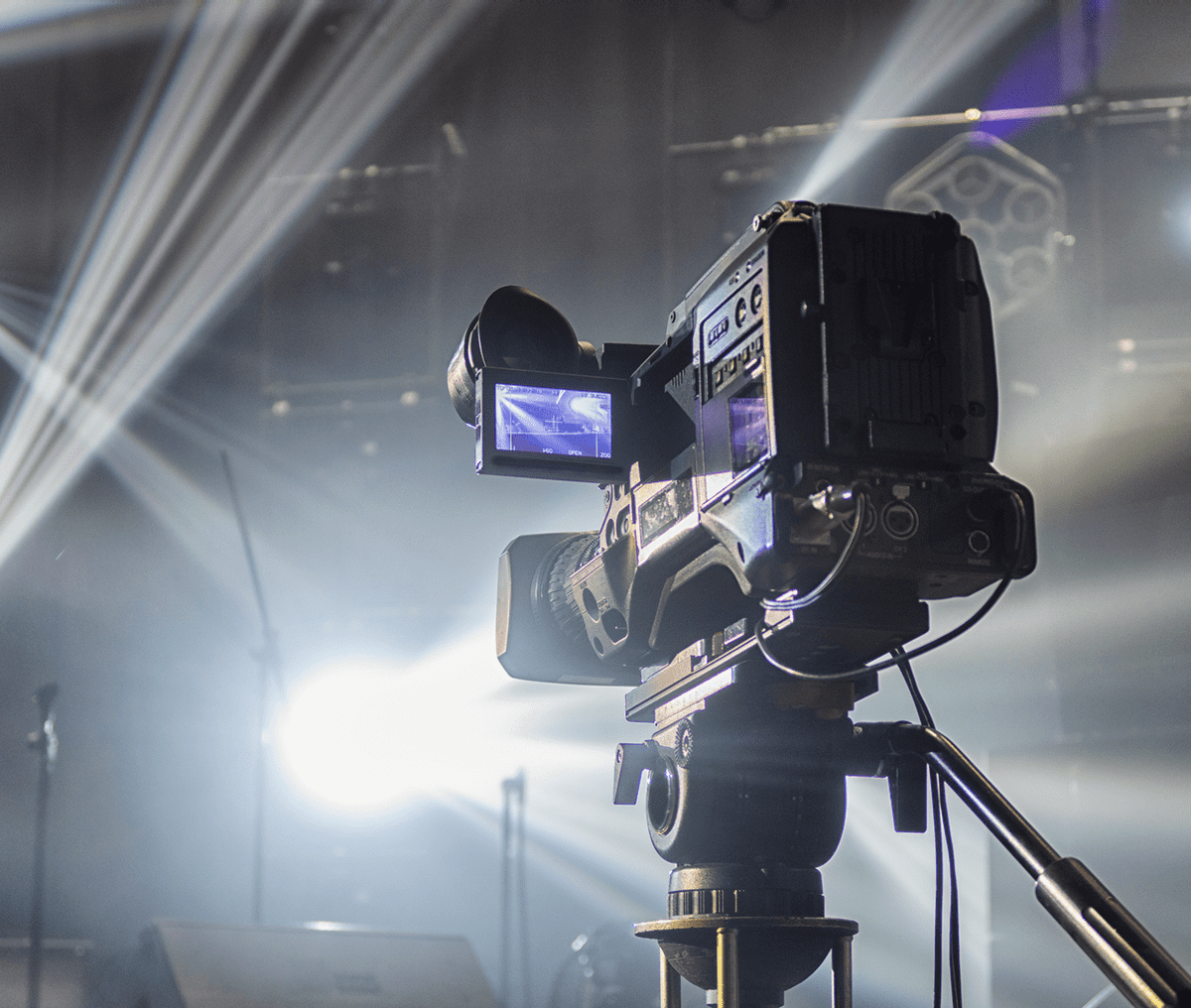 Professional video camera recording a live event with bright stage lights.